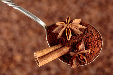Spoon of ground coffee with anise and cinnamon stick on the background of coffee beans.