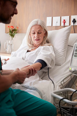 Obraz premium Male Nurse Taking Mature Female Patients Blood Pressure In Hospital Bed With Automated Machine