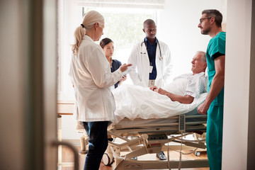 Medical Team On Rounds Meeting Around Bed Of Senior Male Patient