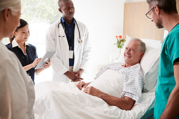 Medical Team On Rounds Meeting Around Bed Of Senior Male Patient