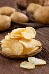 Crispy potato chips on plate with fresh potatoes on wooden table. Appetizer and Snack food.