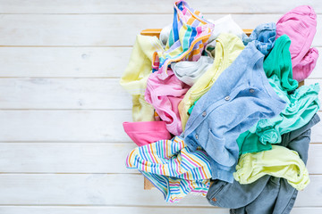 Marie Kondo tyding up method concept - unfolded kids clothes in pastel colors, mess, copy space