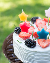 white fruit cake with stars candles on the grass. green background. summer holiday