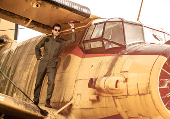 A handsome young pilot standing on the wing of a plane