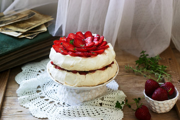 Pavlova meringue homemade cake with strawberries and cream on the background of an old photo album. Rustic style.