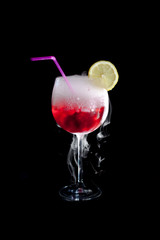 A cup of red cold cocktail with dry ice smoke and a lemon slice