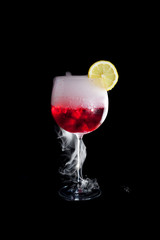A cup of red cold cocktail with dry ice smoke and a lemon slice