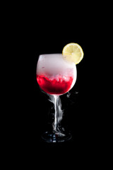A cup of red cold cocktail with dry ice smoke and a lemon slice