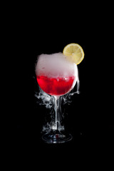A cup of red cold cocktail with dry ice smoke and a lemon slice