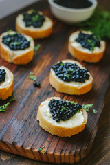 Black caviar on the pieces of bread over wooden kitchen board.