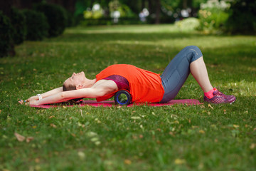 A young woman does stretching with a special roller in the park.