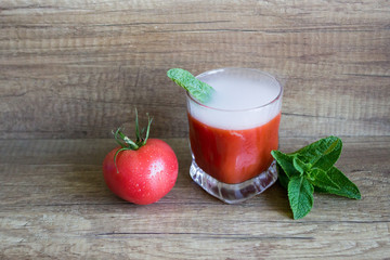Glass of fresh tomato juice and tomatoes on a wooden background
