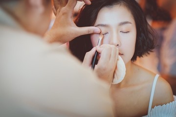  Makeup artist applying pink eyeshadow to beautiful Asian model