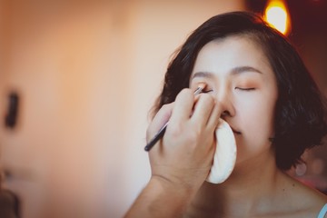  Makeup artist applying pink eyeshadow to beautiful Asian model - obrazy, fototapety, plakaty