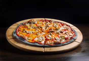 Pizza with jalapeno pepper, dried tomatoes and chicken breast on black dough.