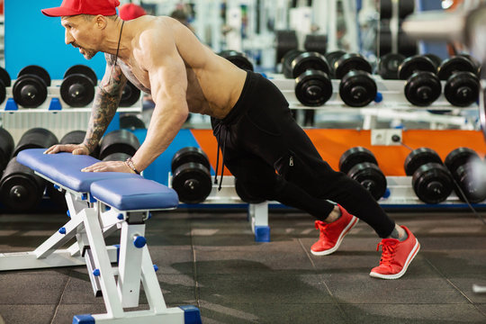 Strong sporty man doing push-ups on bench during workout in gym