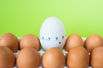 Packed chicken eggs and white timer on a green background. Shelf life. Time and conditions of storage of eggs. To boil eggs.