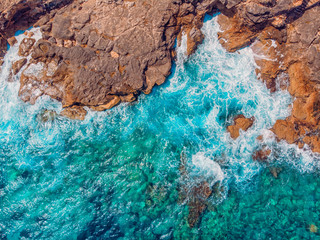Azure clear water hits the rocky coast of coral beach. Aerial top view