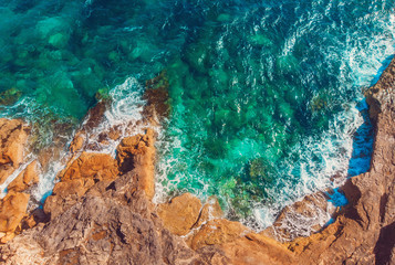 Azure clear water hits the rocky coast of coral beach. Aerial top view