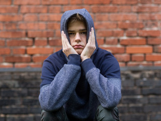 sad, lonely teenager in the hood is sitting on the background of a brick wall