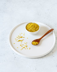Bee pollen in a bowl and wooden spoon on white stone background