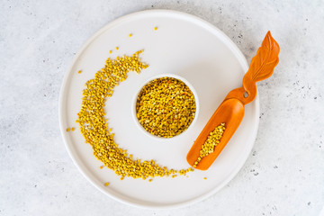 Bee pollen in a bowl and wooden spoon on white stone background