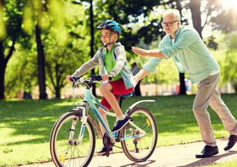 family, generation, safety and people concept - happy grandfather teaching boy how to ride bicycle at summer park