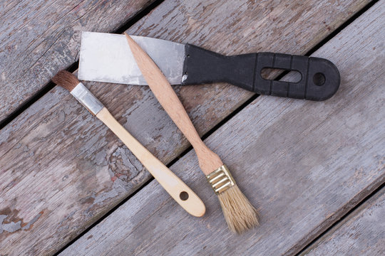 Construction tools on wooden boards background. Metal spatula with plastic handle and two paint brushes on rustic planks.