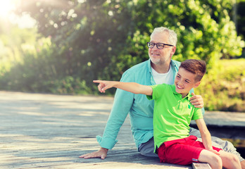 Obraz premium family, generation, communication and people concept - happy grandfather and grandson sitting on river berth