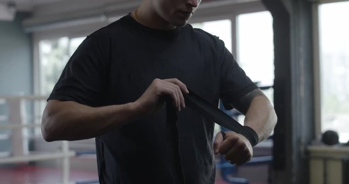 Man wraps his hands with boxing bandages, kickboxing training day in a gym, slow motion.