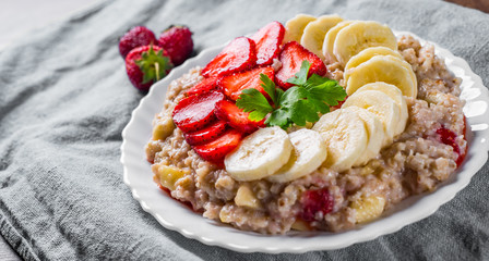 Oatmeal porridge with milk, strawberry, banana in white plate on wooden table background
