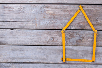 Meter rule folded in form of a house. House shape made from folding ruler on old wooden background. Space for text.