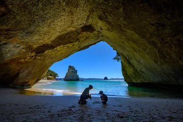 Tuinposter Boy and mother playing under the arch of Cathedral Cove beach, New Zealand North Island © Yann