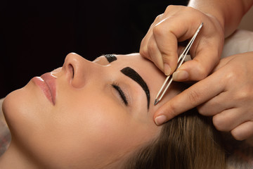 Young woman having professional eyebrow correction procedure in beauty salon