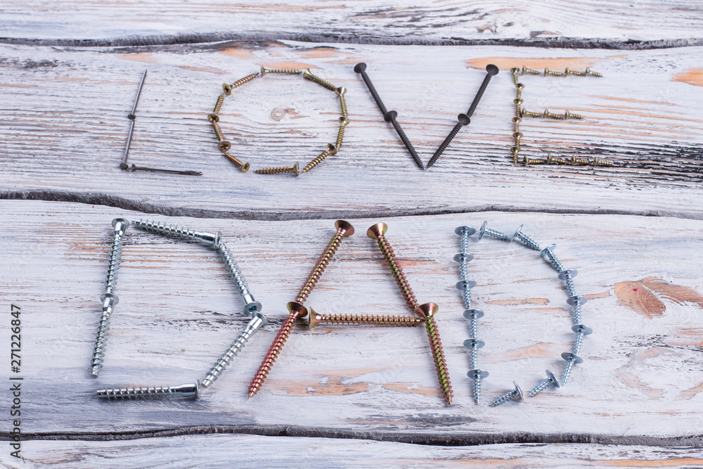 Wall mural Text LOVE DAD on wooden background. Decoration from metal screws and nails for Fathers Day.