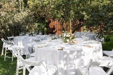 Wedding table setting decorated with fresh flowers in a brass vase. Wedding floristry. Banquet table for guests outdoors with a view of green nature. Bouquet with roses, eustoma and eucalyptus leaves