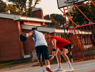 Two young friends playing basketball on court outdoors.