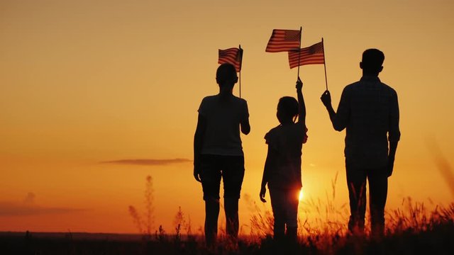 Family with child waving US flags at sunset, rear view