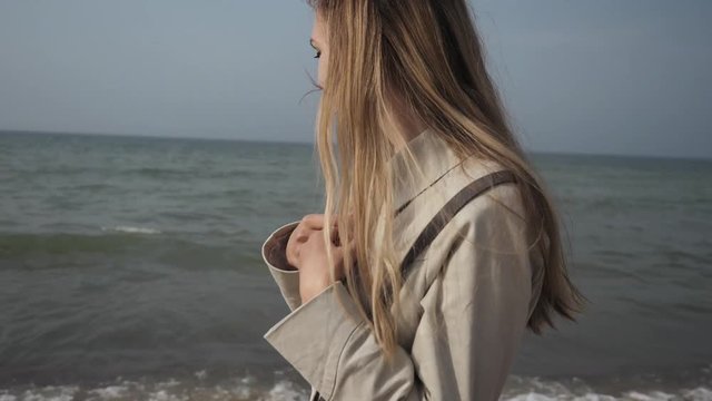 young happy woman with long hair in a beige coat close-up dancing on the sea beach