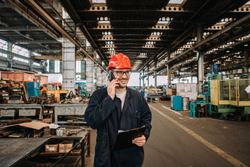 Worker talking on mobile phone at metal manufacturing plant.