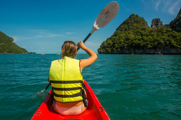 Woman exploring calm tropical bay with limestone mountains by kayak, back view