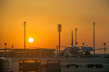 Scenic airplane silhouette parked to air stairs airport trucks air traffic control in front of sun at sunrise