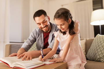 education, family and homework concept - happy father and daughter with book writing to notebook at home