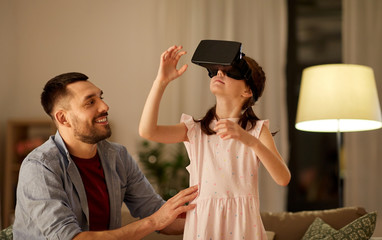 family, virtual reality and entertainment concept - happy father and little daughter with vr glasses playing video game at home in evening