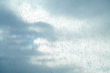 Transparent drops of rain on glass on background of the clear blue sky with clouds closeup on a good summer day