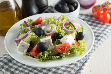 Obraz na płótnie Canvas Fresh Greek salad with delicious ruccola, spinach, cabbage, arugula, feta cheese, red onion and cherry tomato on wooden background. Oil, salt and pepper. Healthy and diet food concept.