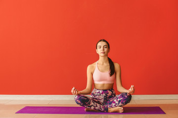 Sporty woman practicing yoga near color wall