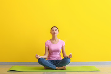 Beautiful woman practicing yoga near color wall