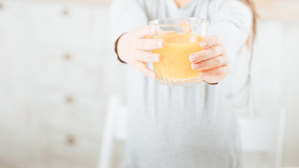 Healthy diet. Balanced nutrition breakfast. Glass of orange juice in kid hands. Blur background. Copy space.
