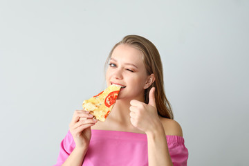 Beautiful woman eating tasty pizza on light background